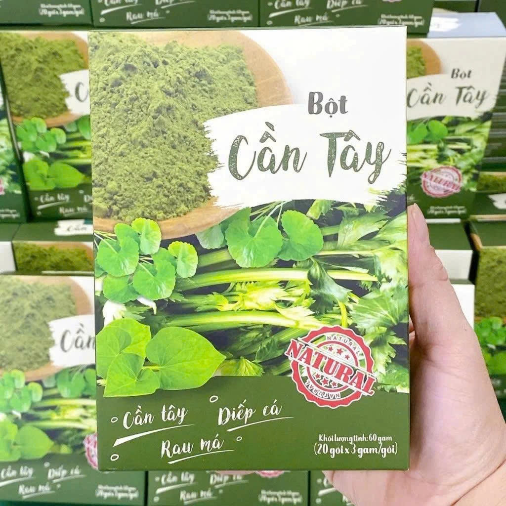 Hộp Bột Cần Tây Rau Má Diếp Cá Mộc Tâm cầm trên tay, phía sau là các hộp xếp chồng
